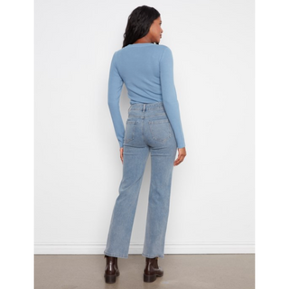 A woman shown from the back wearing a light blue long-sleeve top and light blue high-waisted straight-leg jeans, paired with dark brown boots, against a white wall.