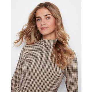 A woman with blonde wavy hair wearing a beige and brown checkered mock neck long-sleeve top, photographed against a light gray studio background.