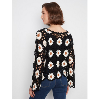 A woman shown from the back wearing a black crochet sweater with a white and tan daisy pattern, paired with blue jeans, against a light gray background.