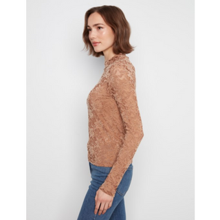 A woman shown in side profile wearing a fitted, long-sleeve lace top in a warm tan/caramel shade, paired with blue jeans, against a plain light gray studio background.