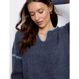 A woman wearing a navy blue knit sweater with light blue scalloped trim around the split neckline and a matching light blue stripe on the sleeve, shown against a plain light background.