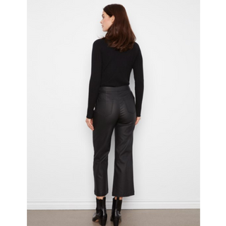 A woman is shown from the back wearing a black ribbed long-sleeve top, black cropped trousers, and black ankle boots against a plain white wall.
