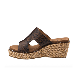 A women's wedge sandal shown in side profile on a white background. The upper is dark brown embossed leather with a cutout design, and the wedge and insole are tan.