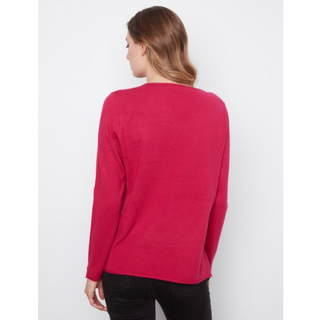 A woman shown from the back wearing a bright pinkish-red long-sleeve knit top and black pants against a plain light gray studio background.