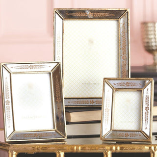 Three rectangular picture frames with ornate gold-toned borders and mirrored backings, arranged on stacked books against a soft pink background.