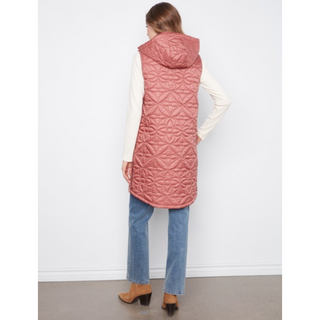 A woman shown from the back wearing a dusty rose quilted puffer vest over a cream long-sleeve top, blue jeans, and brown heeled boots, standing against a plain white wall.