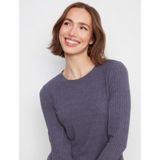 A woman with shoulder-length brown hair smiling and looking upward, wearing a ribbed long-sleeve crewneck sweater in a medium grey color against a light gray background.