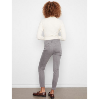 A person shown from the back wearing gray slim-fit ankle-length pants, a cream long-sleeve top, and brown loafers against a plain white wall.