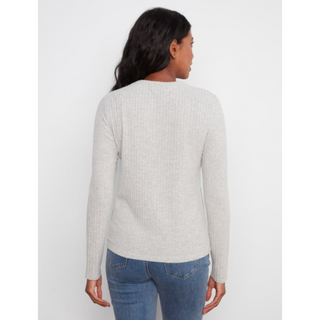 A woman viewed from the back wearing a light gray ribbed knit sweater and blue jeans against a plain light gray studio background.