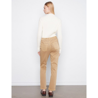 A woman shown from the back wearing a cream mock-neck long-sleeve top and tan straight-leg pants, standing against a white wall.