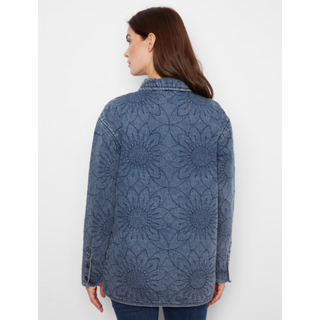 A woman shown from the back wearing a blue denim jacket with a raised sunflower pattern, set against a plain light gray background.