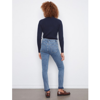 A person shown from the back wearing a dark navy ribbed long-sleeve top, light blue high-waisted skinny jeans, and brown leather loafers, standing against a plain white wall.