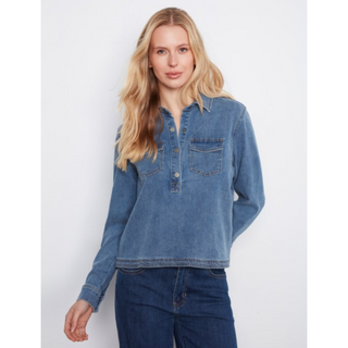 A woman modeling a blue long-sleeve denim shirt with a buttoned henley-style placket and chest pockets, paired with dark blue jeans, against a light gray studio background.