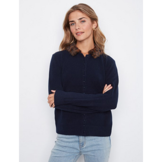 A woman wearing a dark navy blue knit cardigan sweater with a brown faux-fur collar, paired with light blue jeans, standing against a plain light gray background.