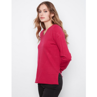A woman modeling a bright pink long-sleeve V-neck knit sweater against a plain light gray studio background.