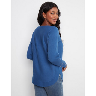 A woman wearing a blue long-sleeve knit top, shown from the back and side against a plain light gray studio background.