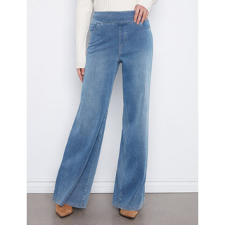 A person wearing light blue wide-leg denim jeans with a cream ribbed sweater and tan shoes, standing against a plain white wall.