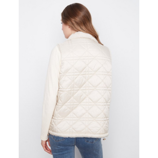 A woman shown from the back wearing a cream-colored quilted puffer vest over a cream long-sleeve top and blue jeans, set against a plain light gray studio background.