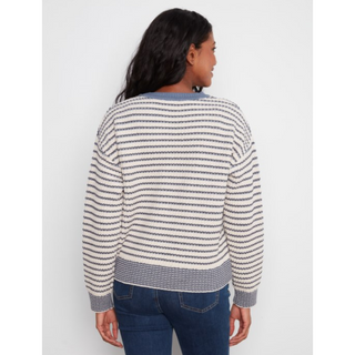 A woman viewed from the back wearing a cream and navy striped knit sweater with blue jeans, set against a plain light gray studio background.