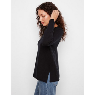 A woman with curly brown hair wearing a black long-sleeve top and blue jeans, shown in profile against a light gray studio background.