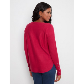 A woman shown from the back wearing a bright pinkish-red knit sweater with lace-up detailing on the sleeves, paired with blue jeans, against a plain light gray background.