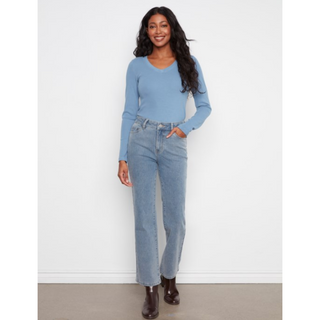 A woman modeling a light blue long-sleeve knit top and light-wash blue straight-leg jeans with brown ankle boots, standing against a plain white wall.