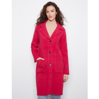 A woman modeling a bright pinkish-red textured coat with a button front, wide lapels, and front pockets, set against a plain light gray background.