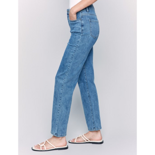 A side-profile view of a person wearing light blue straight-leg denim jeans and beige flat sandals against a light gray studio background.