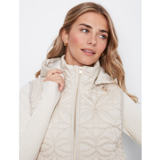 A woman wearing a cream-colored quilted puffer vest over a matching ribbed knit sweater, photographed against a clean white studio background.