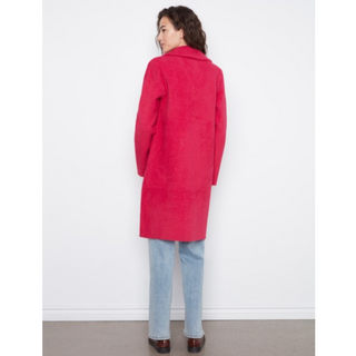 A woman shown from the back wearing a bright pinkish-red mid-length coat, light blue jeans, and brown shoes, standing against a plain white wall.