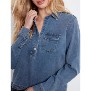 A woman wearing a medium-wash blue denim long-sleeve half-button shirt with chest pockets, shown in a close-up lifestyle shot against a light gray background.