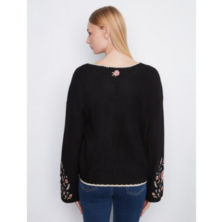 A woman shown from the back wearing a black knit sweater with floral embroidery on the cuffs and a small embroidered detail at the neckline, paired with blue jeans against a light gray background.