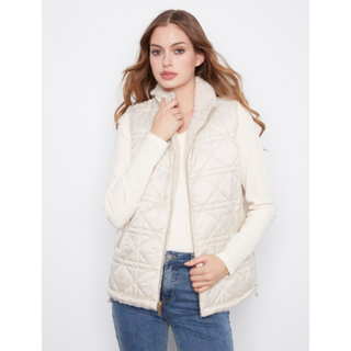 A woman modeling a cream-colored quilted vest over a matching cream top and blue jeans, set against a plain light gray studio background.