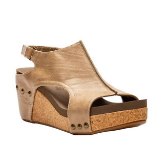A single women's wedge sandal in a light tan leather finish, featuring an open toe, ankle strap, and a cork-textured wedge heel with metal studs, shown against a plain white background.