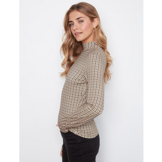 A woman wearing a beige and brown checkered mock neck long-sleeve top, paired with black pants, photographed against a light gray studio background.
