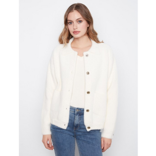 A woman wearing a cream-colored, textured button-up jacket over a matching cream top and blue jeans, photographed against a plain light gray studio background.