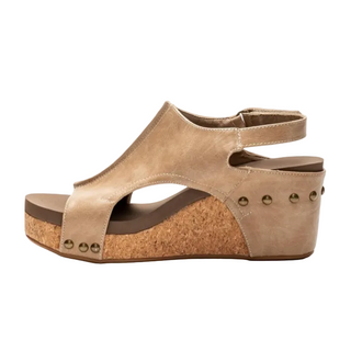A single women's wedge sandal in a light tan suede-like material, featuring an open toe, ankle strap, cork-textured wedge heel, and small metallic studs, shown against a plain white background.