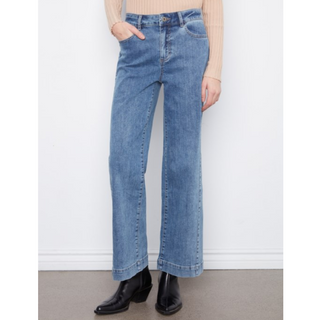 A person wearing light blue wide-leg denim jeans with a beige ribbed knit top and black ankle boots, standing against a plain white wall.