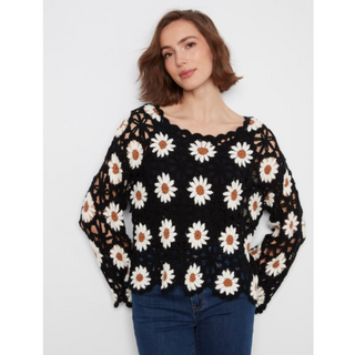 A woman wearing a black crochet knit top with a white and brown daisy pattern, paired with blue jeans, against a light gray background.