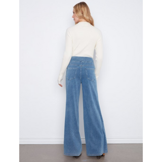 A woman shown from the back wearing a cream ribbed long-sleeve mock neck top and high-waisted, wide-leg blue jeans against a white wall.