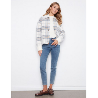 A woman modeling a white cropped plaid jacket with blue and orange lines, paired with blue jeans and brown loafers, standing against a white wall.