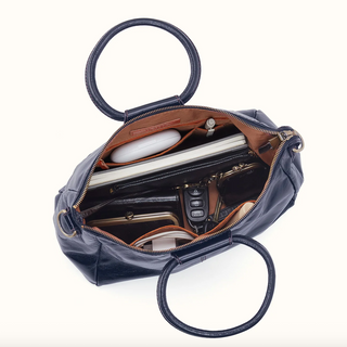 An open navy blue leather handbag with gold-tone hardware, shown from above to reveal its interior compartments filled with travel accessories, on a clean white background.