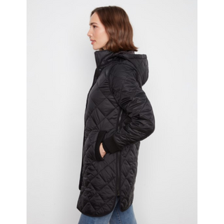 A woman shown in profile wearing a long black quilted puffer jacket with a high collar and hood, paired with blue jeans, against a plain light gray studio background.