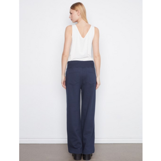 A woman shown from the back wearing navy wide-leg trousers and a white sleeveless top, standing against a plain white wall.