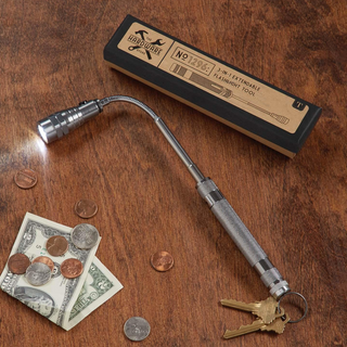 A silver metal flexible flashlight with a keychain ring is displayed on a wooden tabletop next to its black and tan packaging box, along with coins and a dollar bill as props.