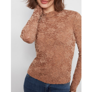 A woman wearing a fitted long-sleeve lace top in a warm tan-brown color, paired with blue jeans, against a plain light gray background.