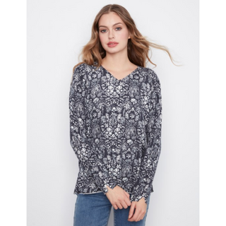 A woman modeling a long-sleeve V-neck sweater with an all-over black and white floral pattern, paired with blue jeans, against a plain light gray background.