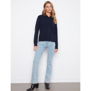 A woman modeling a dark navy long-sleeve knit top with a collar, paired with light-wash blue jeans and black ankle boots, standing against a plain white wall.