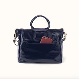 A dark navy blue leather handbag with a top handle and a front pocket containing a reddish-brown phone case, photographed against a plain off-white background.