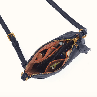 A navy blue leather crossbody bag with gold-tone hardware, shown open to display its interior compartments, tan lining, and tassel zipper pull on a clean white background.